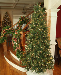 A christmas tree next to a staircase with garland on the railing